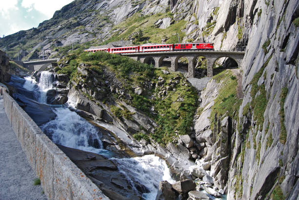 Train of the Matterhorn Gotthard Bahn Andermatt, Uri, Switzerland - September 11, 2011: A push-pull train of the Matterhorn Gotthard Bahn from Andermatt to Göschenen passes the he Devil's Bridge  and disappears in the 306 m long Brüggwald tunnel. lepontine alps stock pictures, royalty-free photos & images