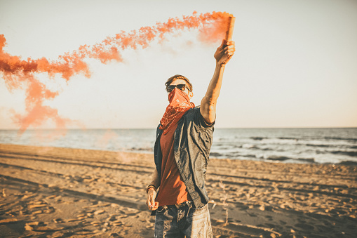 Riot Hipster Man holding red smoke on the beach