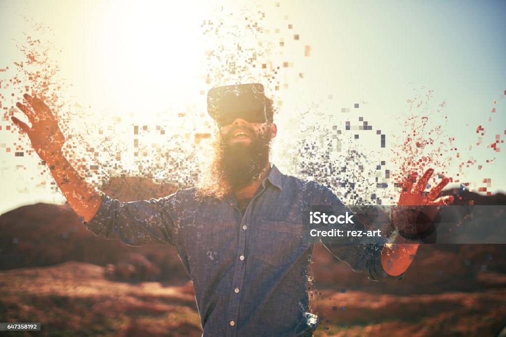 bearded guy in desert wearing vr glasses bearded guy in desert wearing vr glasses dissolving into pixels Sensory Perception Stock Photo