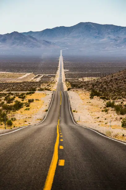 Classic vertical view of an endless straight road running through the barren scenery of famous Death Valley with extreme heat haze on a beautiful sunny day with blue sky in summer, California, USA