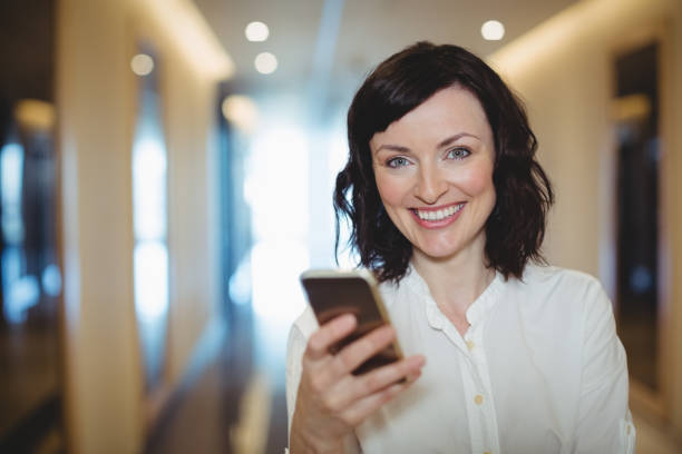 istock Portrait of female executive using mobile phone in corridor 647384378