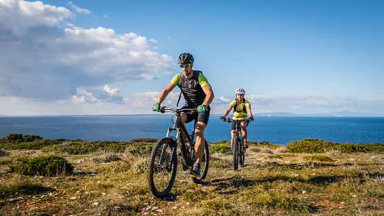 Young couple mountain biking on landscape, sea in background.