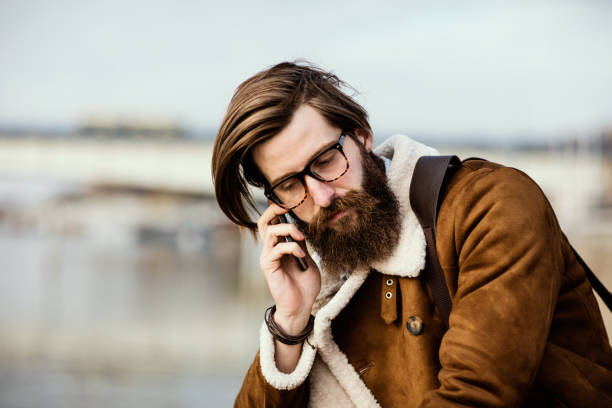 handsome unshaved man with long hair talking on the phone - stubble men tattoo sensuality imagens e fotografias de stock