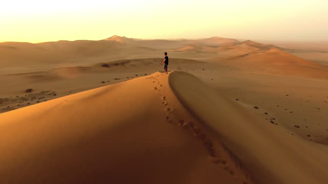 ナミビア砂漠の砂丘を歩く孤独な男の4k空中ドローン映像