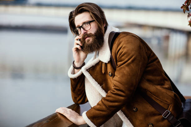 hombre guapo de pelo largo se inclinó cerca hablando por teléfono - stubble men tattoo sensuality fotografías e imágenes de stock