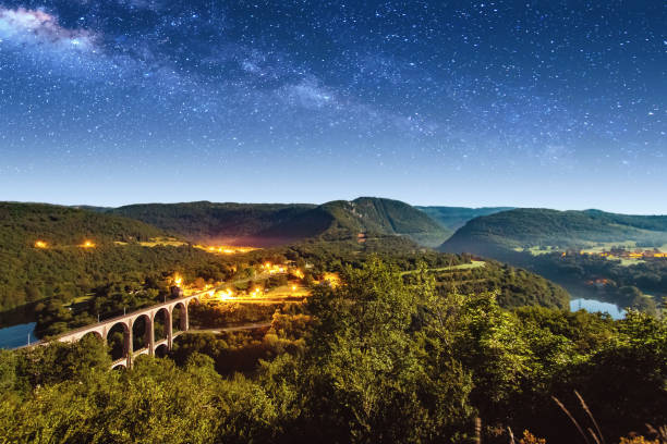 Photo of High angle view of french Bugey mountains beginning of Jura landscape by summer night with old stone railway viaduct arch bridge crossing Ain river and beautiful star sky