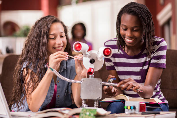 High school girls work on robot for education, engineering science project. Multi-ethnic team of high school age girls work on engineering science project at home.  Mom looks on in background at the robot they created. school science project stock pictures, royalty-free photos & images