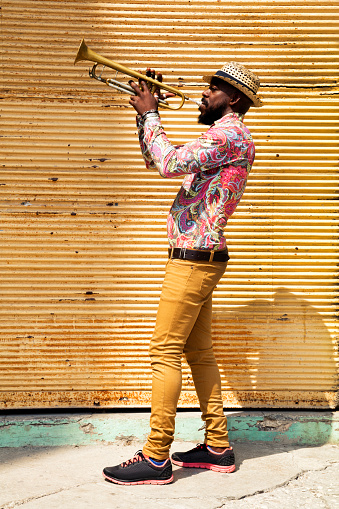 Cuban musician standing against a closed yellow store shutter, playing a trumpet in Havana