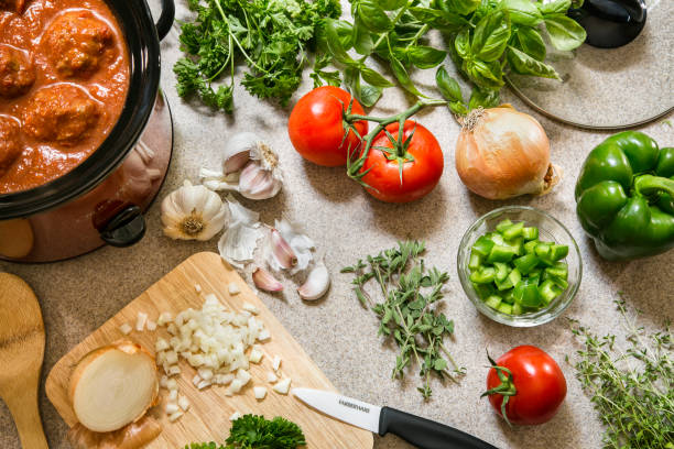 Preparing Dinner with Fresh Foods Preparing meatballs in a crock pot and prepping fresh vegetables for the rest of the meal, including tomatoes, garlic, onion, peppers and fresh herbs. tarragon cutting board vegetable herb stock pictures, royalty-free photos & images