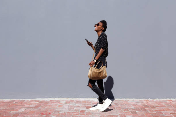 istock Smiling black woman walking outdoors with mobile phone 647437232