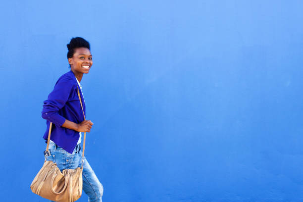 istock Smiling young african woman walking against blue wall 647437366