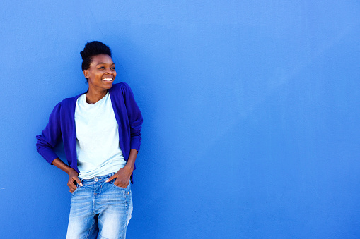 Portrait of happy young african female standing against blue wall with copy space