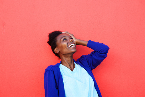 Portrait of young african female laughing with her hand on head against red background