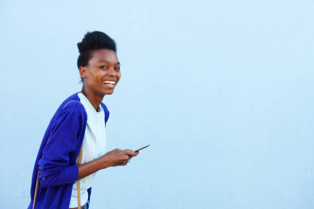 istock Smiling young female model walking with cell phone 647437512
