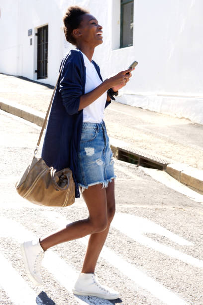 istock Smiling african woman walking with cell phone 647437630