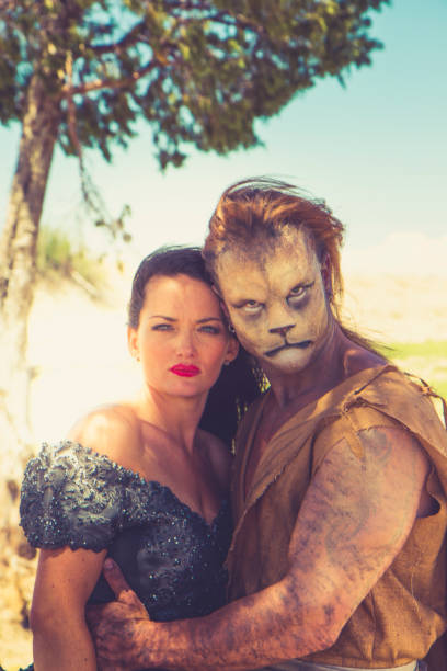 Fantasy man enchanted prince. Ram's horns on head, hugging a beautiful woman by shoulders. Girl in yellow medieval historical dress vintage gown. dark room. Guy beast monster. Story of fairy tale love