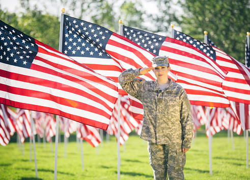 American soldier in uniform saluting while standing in a field of American flags