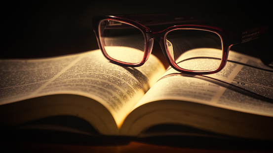 Bible and reading glasses, warm ambient light.