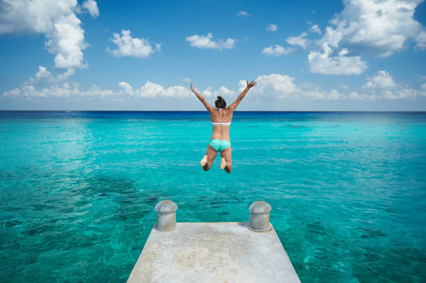 One woman jump in blue water from pier view from back on caribbean vacation
