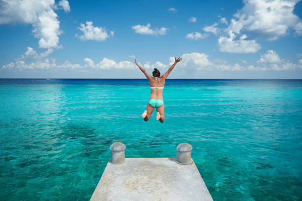 One woman jump in blue water One woman jump in blue water from pier view from back on caribbean vacation incidental people photos stock pictures, royalty-free photos & images