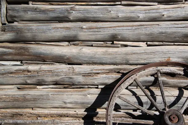 Wagon wheel against Hand cut logs from historic old cabin