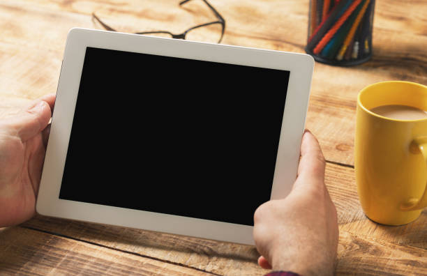 istock Male hands holding a white tablet with copy space sitting on a wooden table 647537808