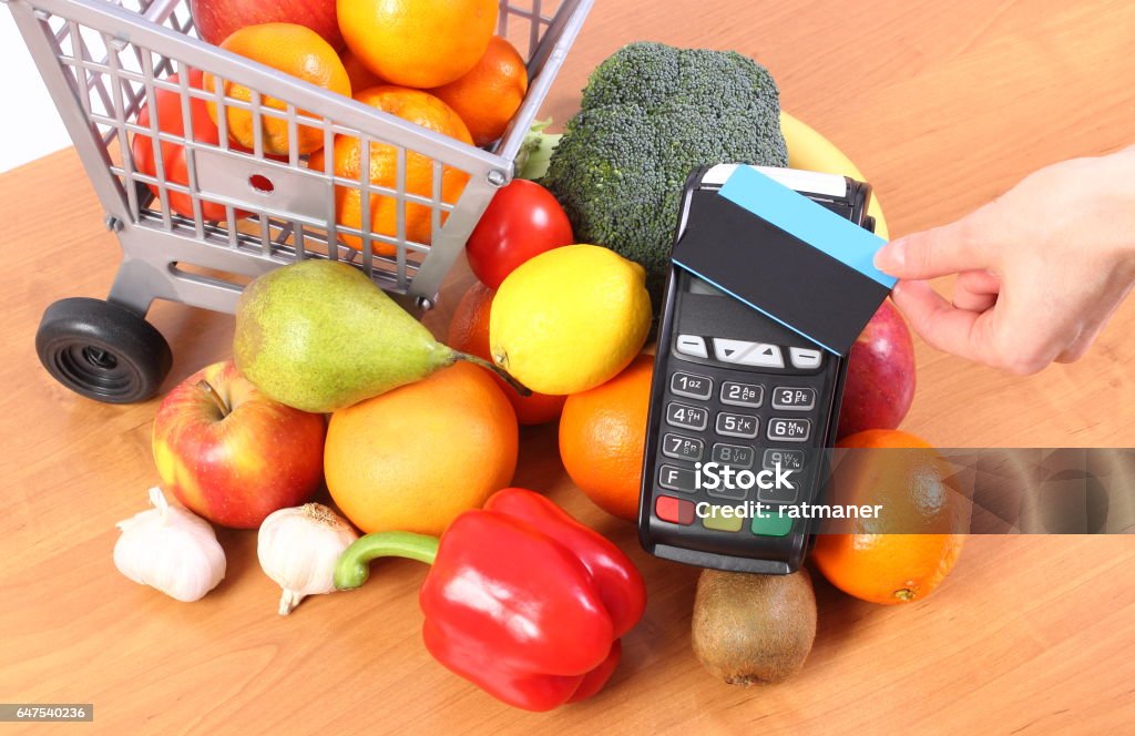 Payment terminal with contactless credit card and fruits and vegetables Using credit card reader, payment terminal with contactless credit card and fresh fruits and vegetables with plastic shopping carts, cashless paying for shopping Apple - Fruit Stock Photo