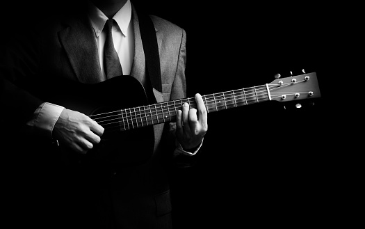 male musician in suit playing acoustic guitar, isolated on black