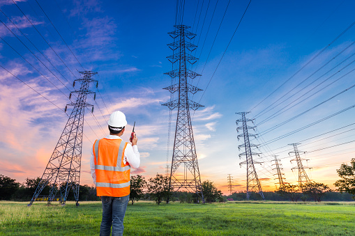 Electrical engineer with high voltage electricity pylon at sunrise background