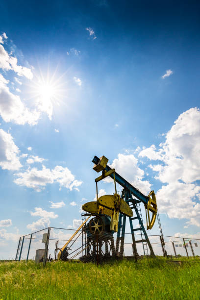 oil field with pump jack, profiled on blue sky with white clouds, on a sunny day - oil pump oil industry alberta equipment imagens e fotografias de stock