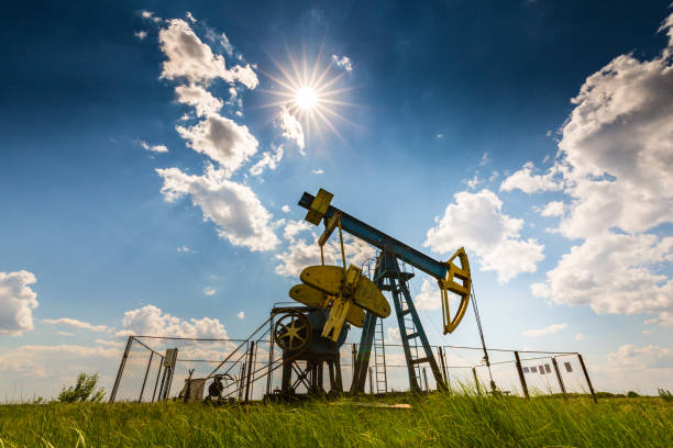 oil field with pump jack, profiled on blue sky with white clouds, on a sunny day - oil pump oil industry alberta equipment imagens e fotografias de stock