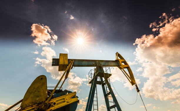 oil field with pump jack, profiled on blue sky with white clouds, on a sunny day - oil pump oil industry alberta equipment imagens e fotografias de stock