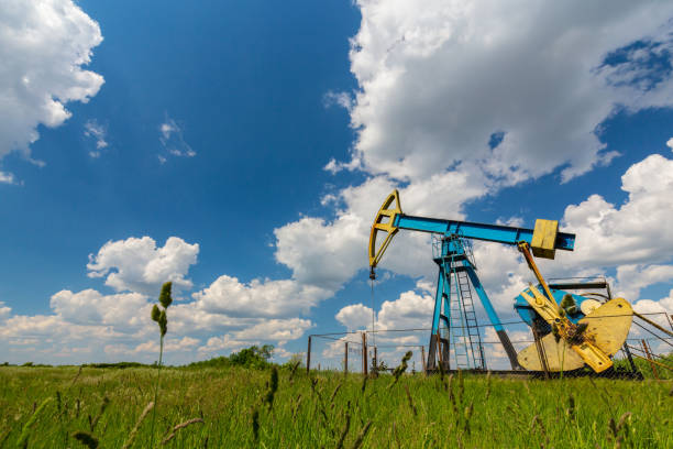 campo de petróleo com tomada de bomba, perfilado no céu azul com nuvens brancas, em um dia ensolarado - oil pump oil industry alberta equipment - fotografias e filmes do acervo