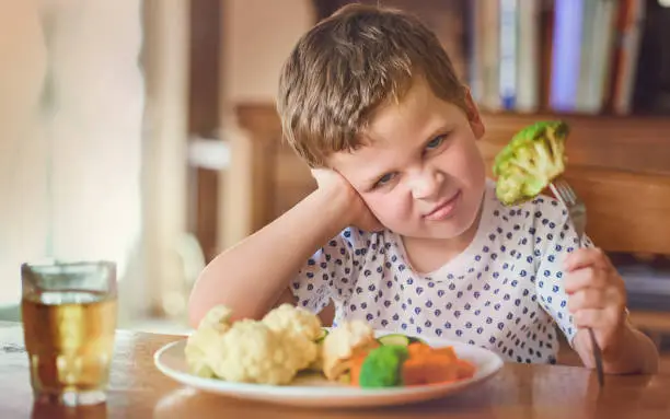 Portrait of a disgusted little boy refusing to eat his vegetables at the dinner table