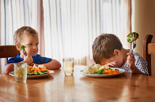 Shot of two unhappy little boys refusing to eat their vegetables at the dinner table
