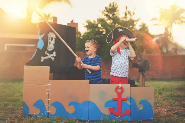 Shot of a cute little boy and his brother playing pirates outside on a boat made of cardboard boxes