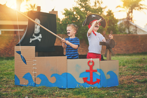 Shot of a cute little boy and his brother playing pirates outside on a boat made of cardboard boxes