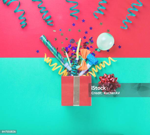 Red Gift Box With Various Party Confetti Balloons Streamers Noisemakers And Decoration On A Multicolored Background Stock Photo - Download Image Now