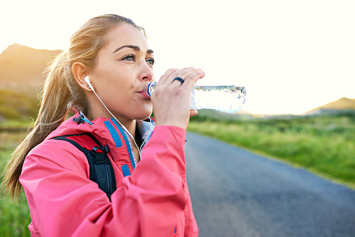Shot of a young woman drinking from a water bottle while taking a break from an early morning run