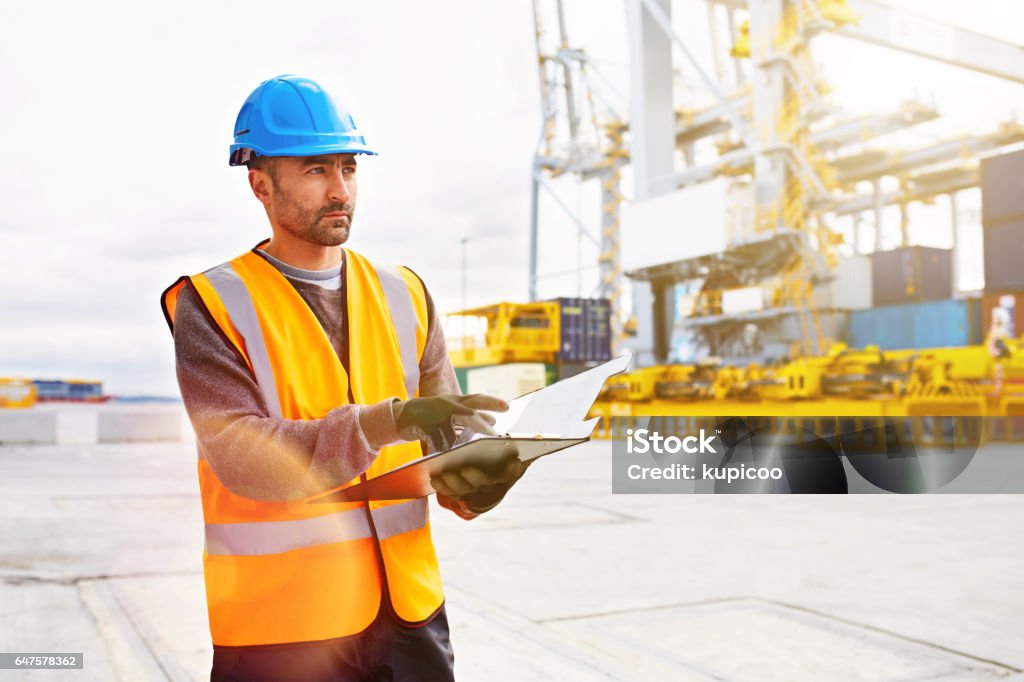 Tracking shipments on the dock Shot of a young man in workwear with a clipboard  Dock Worker Stock Photo