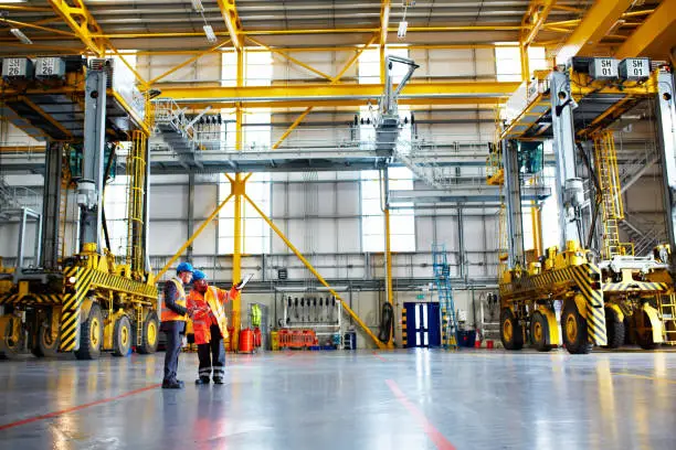 Shot of two warehouse workers talking together over a clipboard inside of a large warehouse