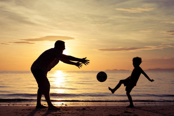 Father and son playing on the beach at the sunset time. Concept of friendly family.