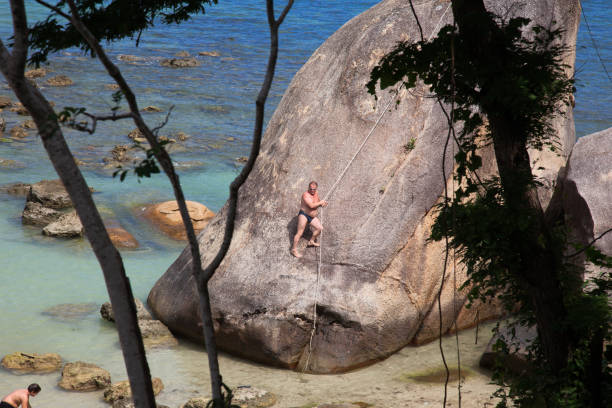 koh samui, tailândia - 12 de janeiro de 2011: homem sobe em um paralelepípedo gigante na praia - homem sunga - fotografias e filmes do acervo