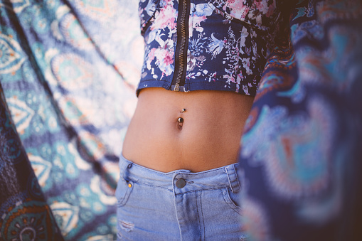 Young slim female model's waist in a crop top and jeans against colorful scarf outdoors in summer