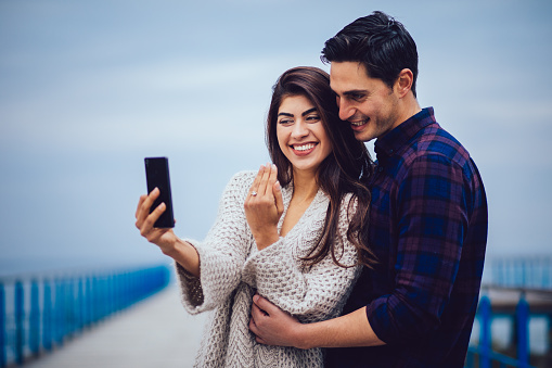 Happy couple taking selfie with engagement ring after wedding proposal. Couple taking photo with engagement ring.