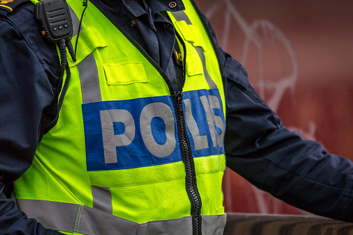 Close up of Swedish police officer wearing a luminous yellow green vest with police text. Only upper body visible, no recognizable person.