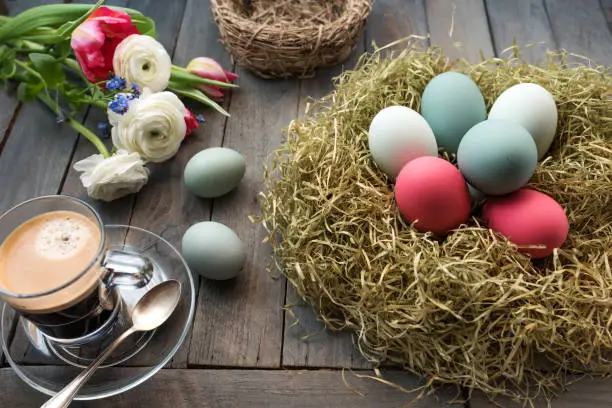 Still life with coffee and colorful easter eggs in a nest on a old shabby wooden table