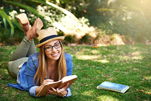 Portrait of an attractive young woman reading a book while lying outside on the grass