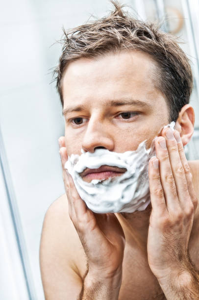istock Man is putting shaving cream on face, bathroom interior 647653236