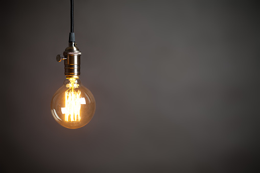 Vintage incandescent Edison type bulb on grey wall. On right is empty space to put text or something else. This file is cleaned and retouched.